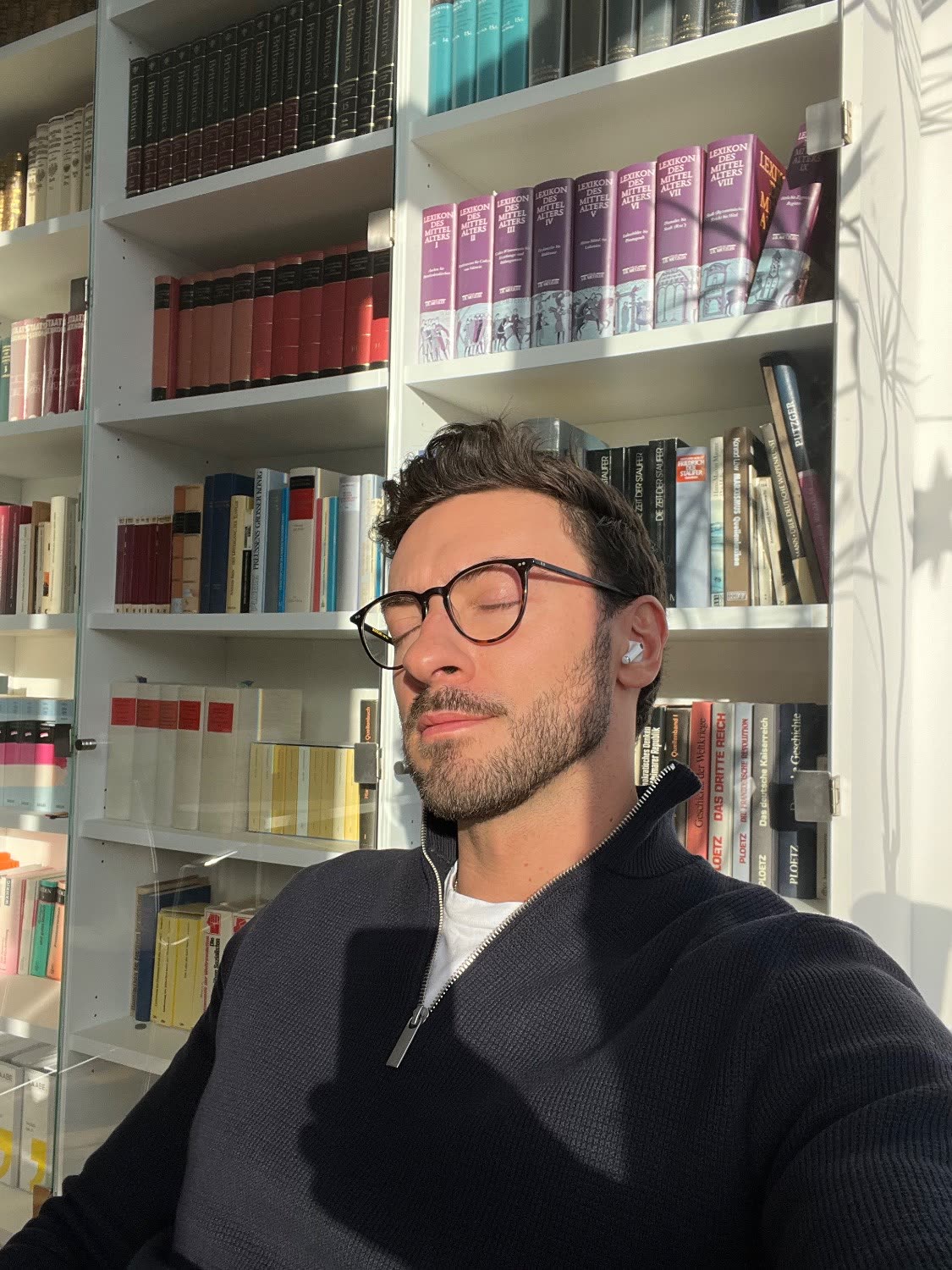 Benni sitzt mit geschlossenen Augen in der Sonne vor einem Bücherregal